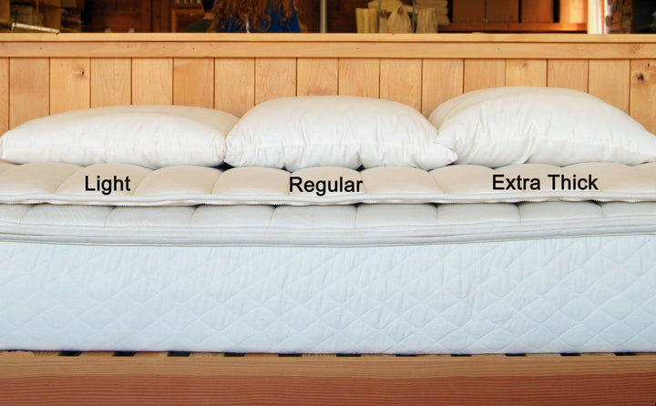 Light, Regular, and Extra Thick Holy Lamb Wool Filled Bed Pillows displayed on a bed mattress.