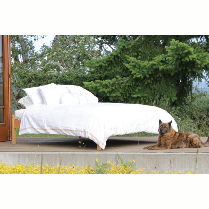 Soaring Heart Organic Cotton Wool Futon full size mattress on a wooden platform surrounded by nature and a dog.