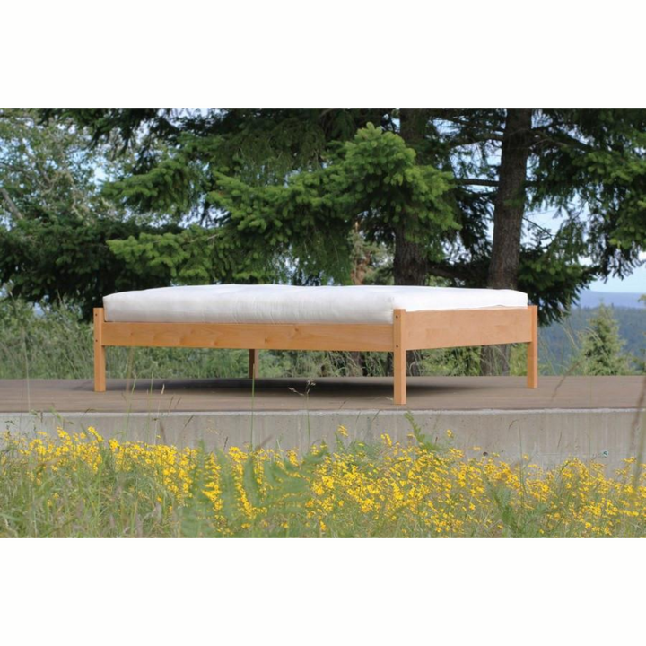 Soaring Heart Organic Cotton Wool Futon on a wooden platform surrounded by greenery and yellow flowers.