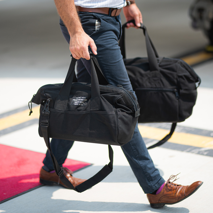 Person carrying two Faraday Cordura Utility Bags in black, demonstrating durable and waterproof construction.